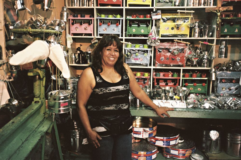 Dueña de una ferretería sonriendo junto a su mostrador lleno de artículos de metal